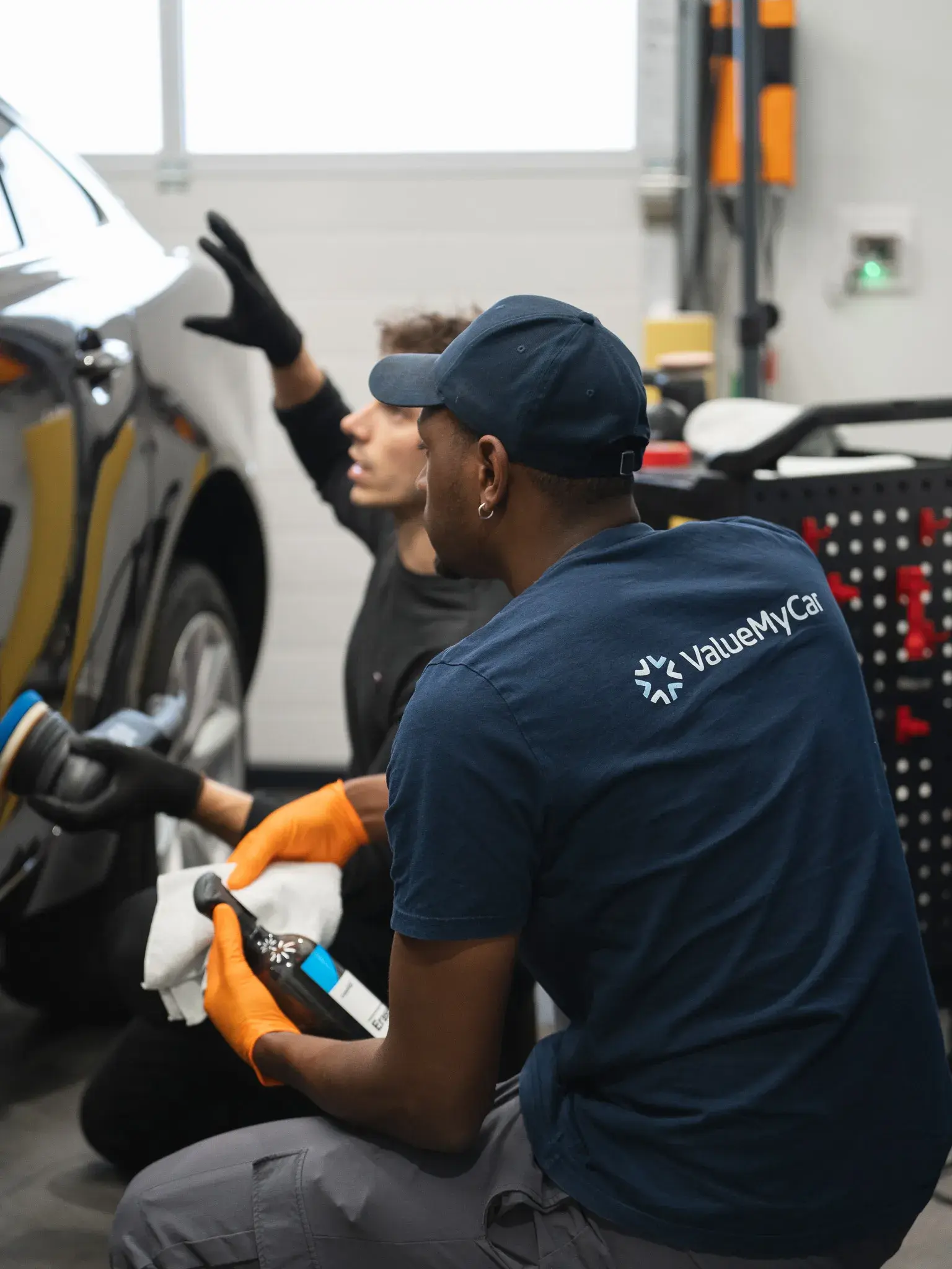 Deux membres de l’équipe ValueMyCar polissent la carrosserie d’une voiture dans un box du centre