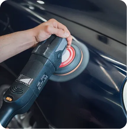Une main guide une polisseuse orbitale sur la carrosserie bleu nuit d’une voiture