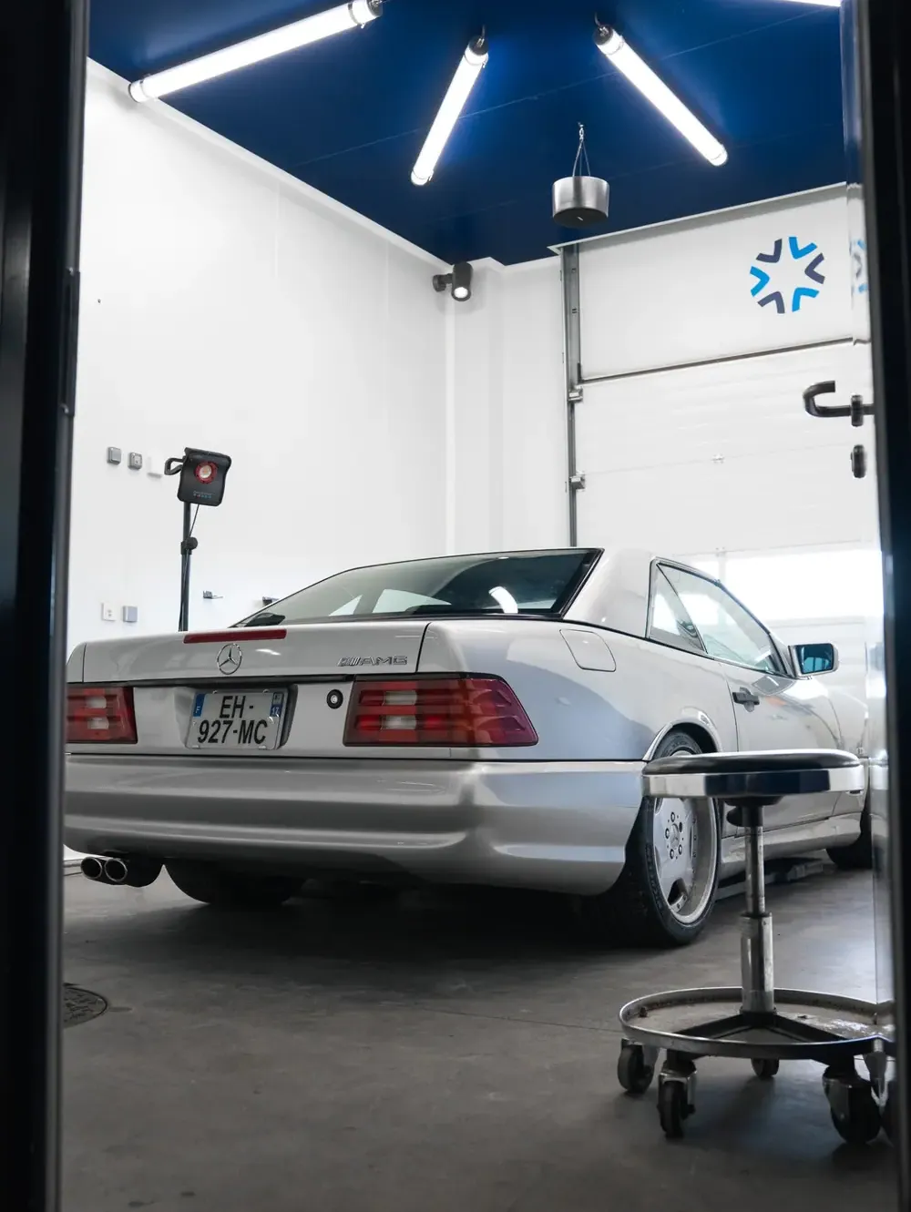 Une Mercedes argentée dans un box detailing aux murs blancs et au plafond bleu éclairé de néons