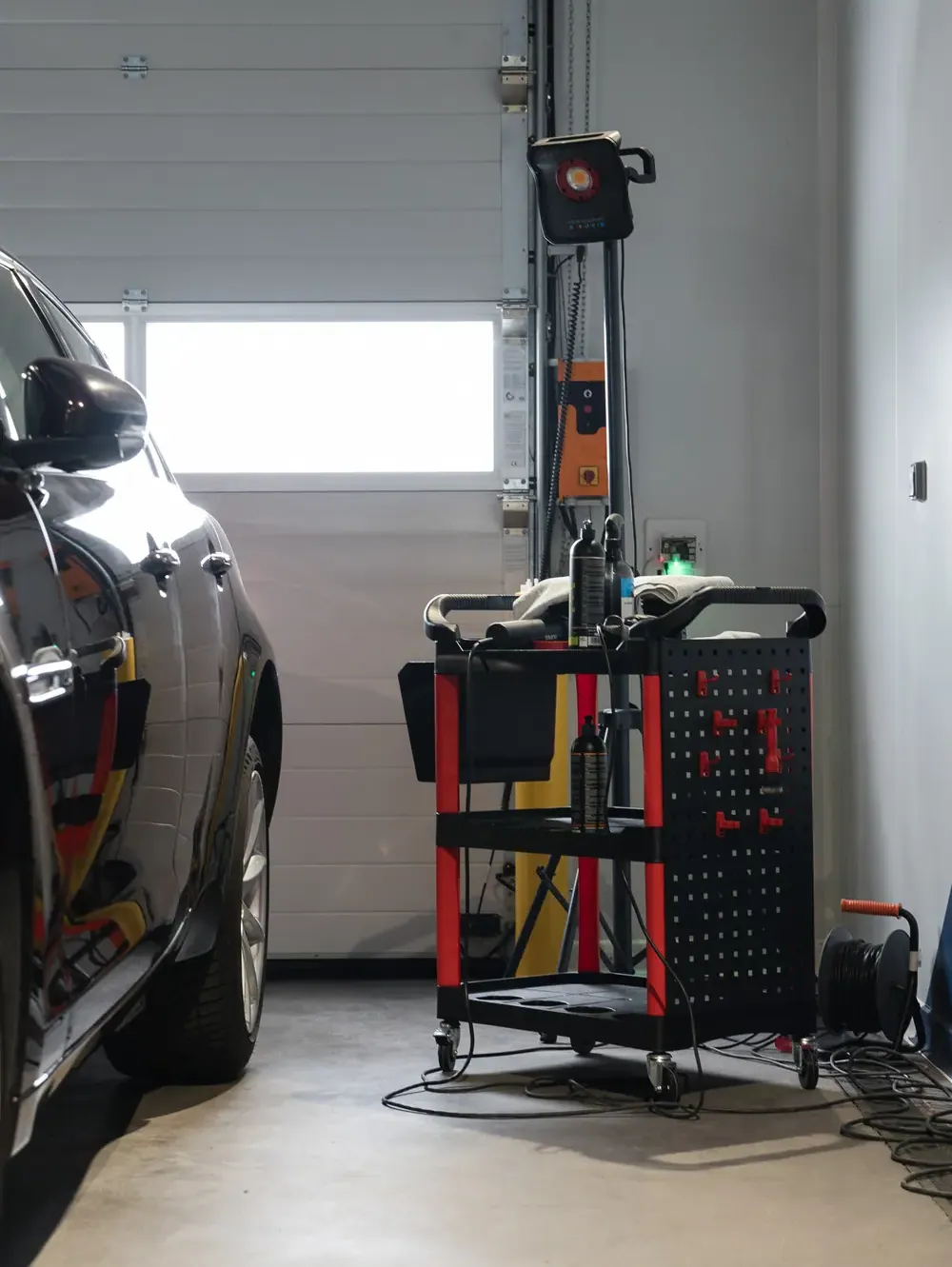 Chariot de produits de detailing et lampe d’inspection, à côté d’une voiture noire dans un box