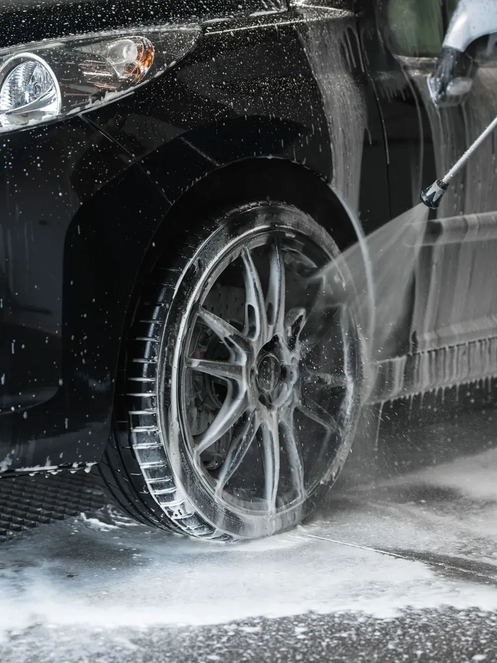 Une roue noire recouverte de mousse, rincée à la lance haute pression