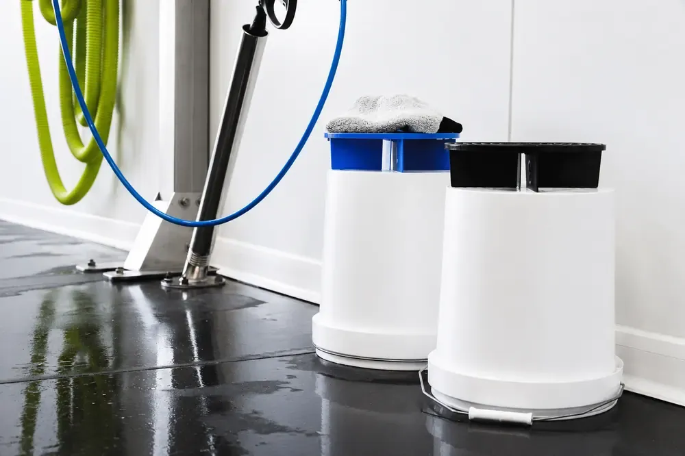 Deux seaux de lavage avec grille anti-gravillons et un enrouleur de tuyau haute pression dans un box