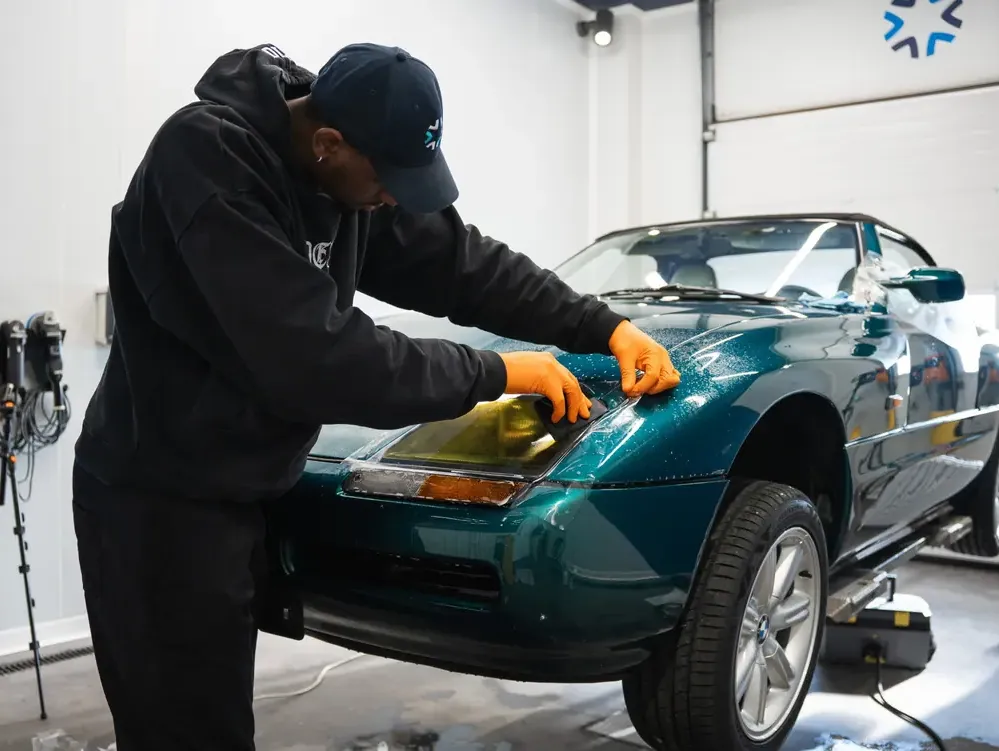 Un professionnel pose un film de protection sur le phare d’un cabriolet BMW vert